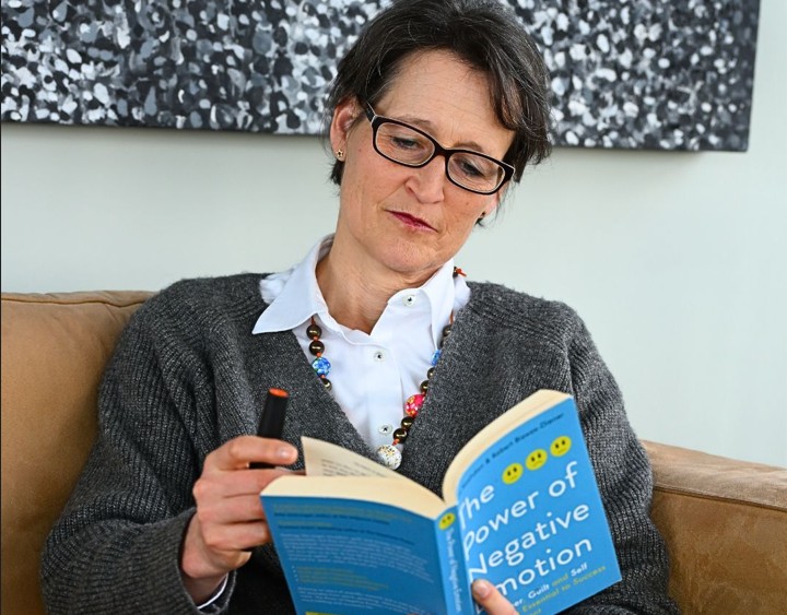 Herdin sitzt auf dem Sofa und studiert das Buch "Power of negative Emotions". Weiterbildung. Wissen.